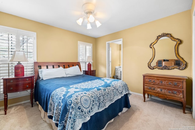 bedroom featuring light carpet, ensuite bathroom, a ceiling fan, and baseboards