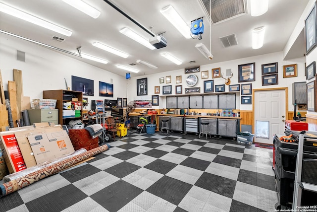 garage with a workshop area, wainscoting, visible vents, and a garage door opener