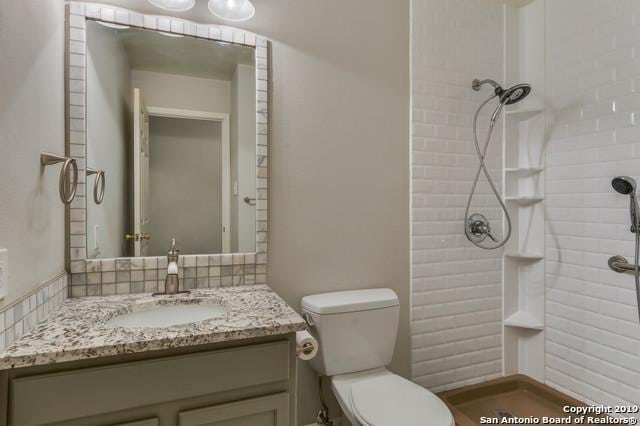 bathroom featuring toilet, tiled shower, and vanity