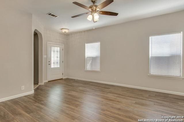 unfurnished room featuring baseboards, visible vents, arched walkways, ceiling fan, and wood finished floors