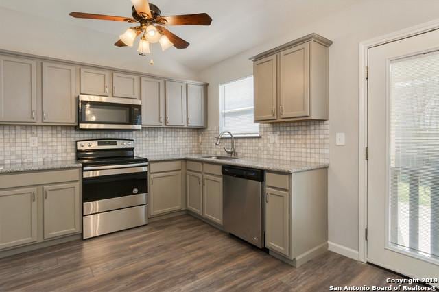 kitchen featuring dark wood finished floors, stainless steel appliances, gray cabinets, decorative backsplash, and a sink