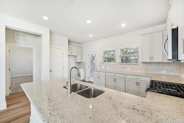 kitchen with a sink, visible vents, white cabinetry, light stone countertops, and stainless steel microwave