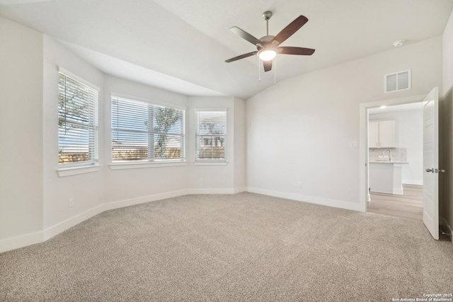 empty room featuring lofted ceiling, light carpet, a sink, visible vents, and baseboards