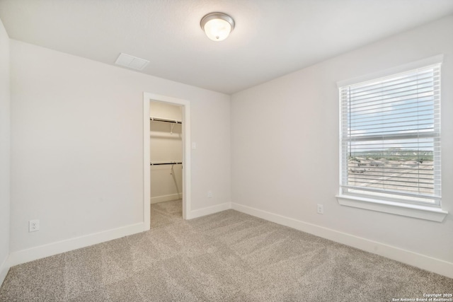 unfurnished bedroom featuring light carpet, multiple windows, baseboards, and a walk in closet