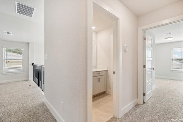 hall with baseboards, visible vents, and light colored carpet