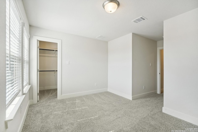 unfurnished bedroom featuring light colored carpet, visible vents, baseboards, a closet, and a walk in closet