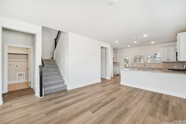 kitchen with a sink, white cabinets, light countertops, decorative backsplash, and light wood finished floors