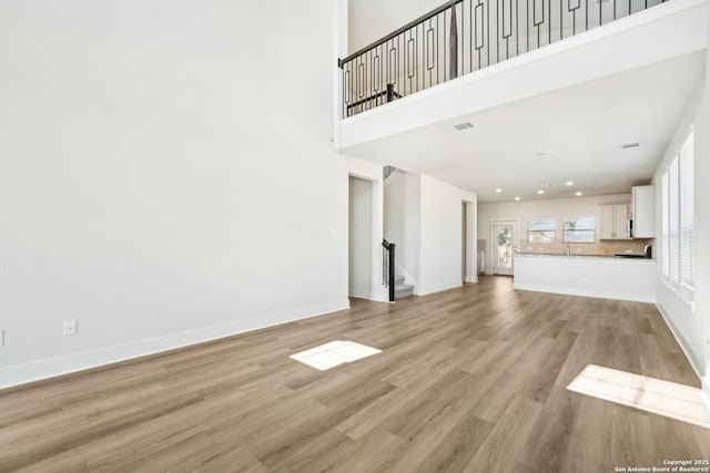 unfurnished living room with light wood-style floors, visible vents, a high ceiling, and baseboards