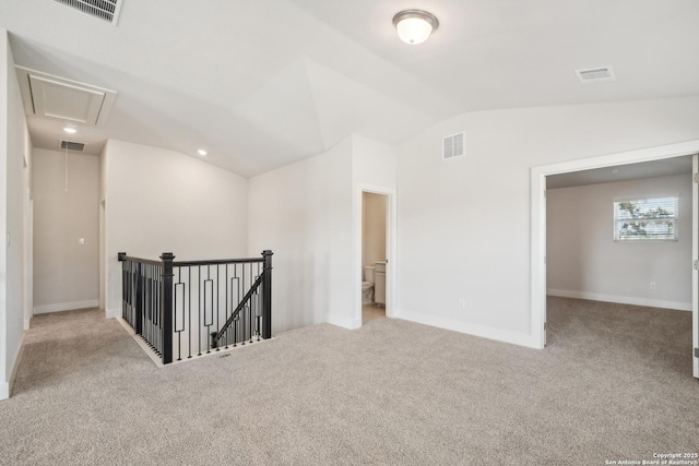 spare room featuring light carpet, attic access, visible vents, and vaulted ceiling