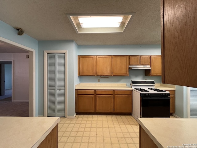 kitchen with under cabinet range hood, light countertops, light floors, brown cabinetry, and gas stove