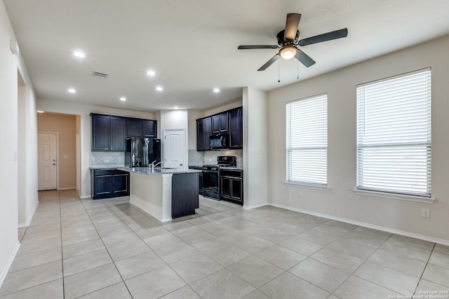 kitchen with tasteful backsplash, visible vents, baseboards, a kitchen island with sink, and black appliances