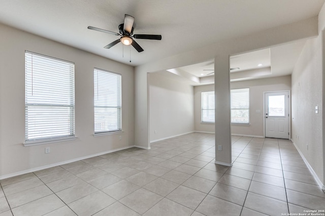 unfurnished room with a healthy amount of sunlight, ceiling fan, a raised ceiling, and light tile patterned flooring