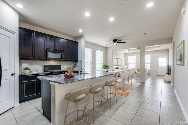 kitchen with decorative backsplash, a kitchen breakfast bar, dark stone countertops, black appliances, and a sink