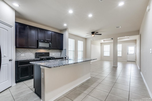 kitchen featuring tasteful backsplash, stone countertops, black appliances, and light tile patterned floors