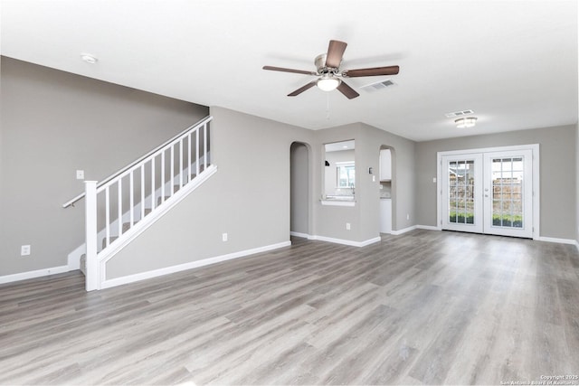 unfurnished living room featuring stairs, arched walkways, visible vents, and light wood-style floors