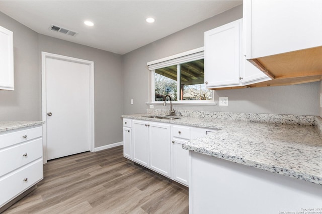 kitchen with visible vents, light stone countertops, light wood-type flooring, white cabinetry, and a sink