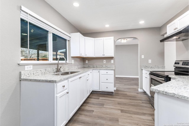 kitchen featuring arched walkways, white cabinets, light wood-type flooring, stainless steel range with electric stovetop, and a sink