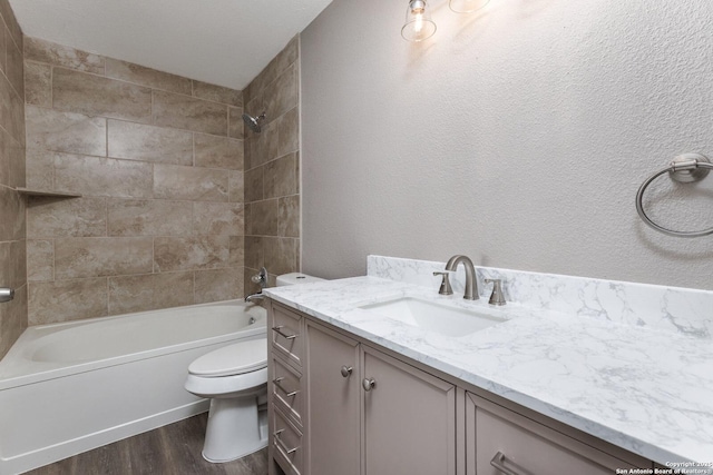 bathroom featuring shower / bathtub combination, a textured wall, toilet, wood finished floors, and vanity