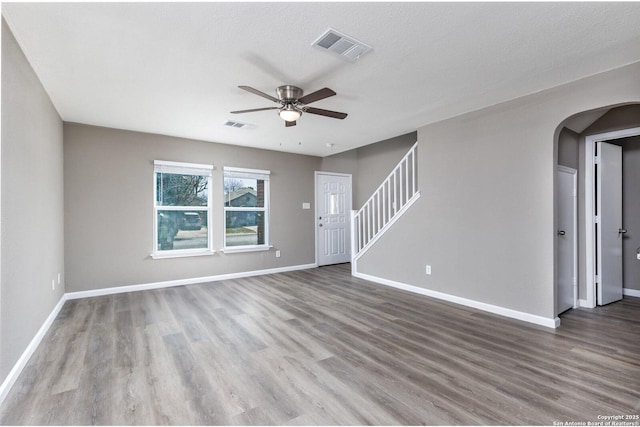 unfurnished living room with visible vents, stairway, and wood finished floors