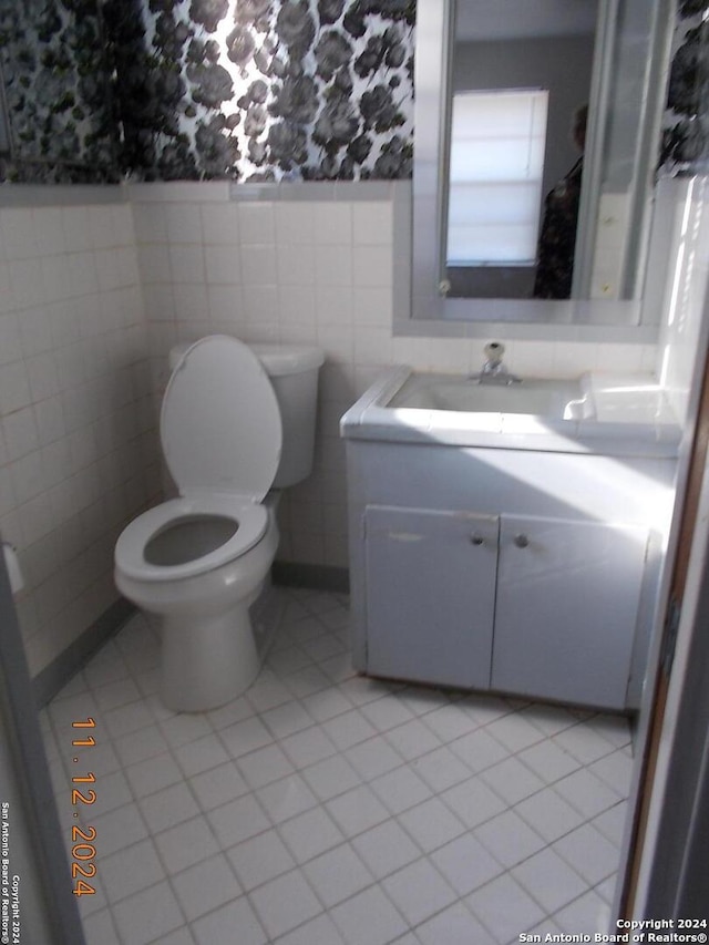 half bathroom with wainscoting, toilet, tile patterned flooring, vanity, and tile walls