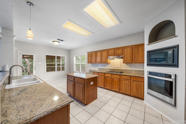 kitchen featuring under cabinet range hood, stainless steel appliances, a kitchen island, a sink, and pendant lighting