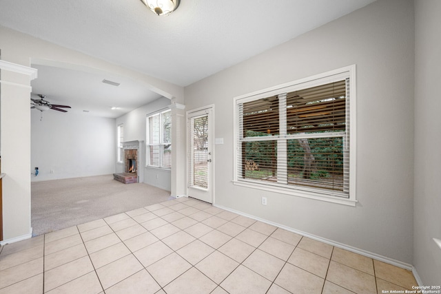 spare room featuring visible vents, light tile patterned floors, a fireplace, and a ceiling fan