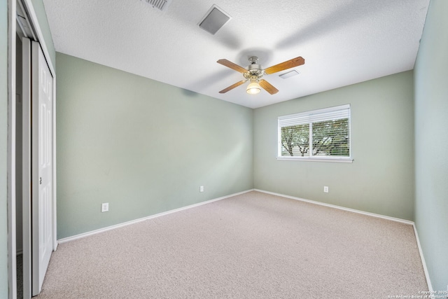 empty room featuring visible vents, light colored carpet, ceiling fan, a textured ceiling, and baseboards