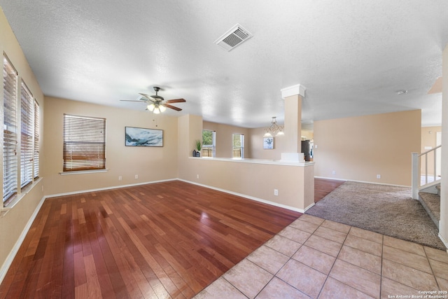 unfurnished living room with stairway, visible vents, wood finished floors, and ceiling fan with notable chandelier