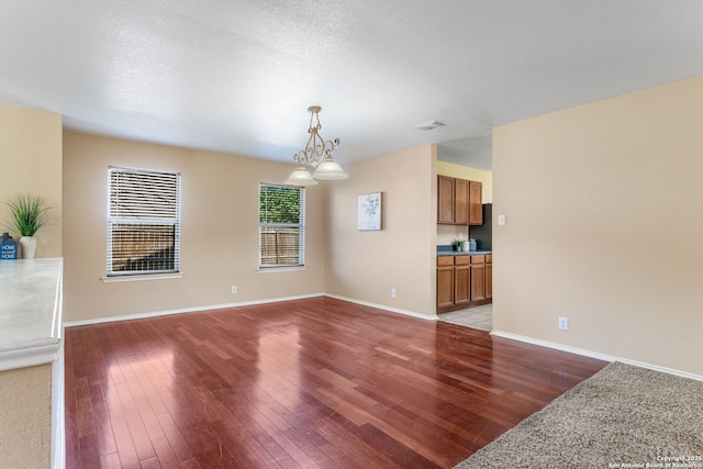 unfurnished living room with baseboards, a textured ceiling, visible vents, and wood finished floors