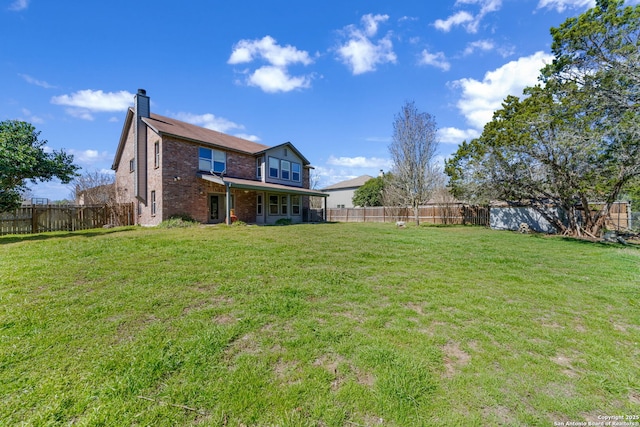 back of house with a yard, a fenced backyard, a chimney, and brick siding