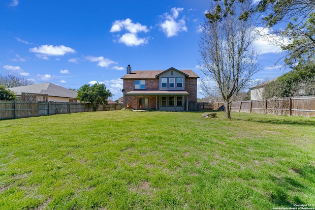 back of house featuring a fenced backyard, a chimney, a lawn, and brick siding