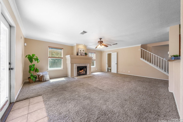 unfurnished living room with a warm lit fireplace, light carpet, visible vents, ornamental molding, and stairway