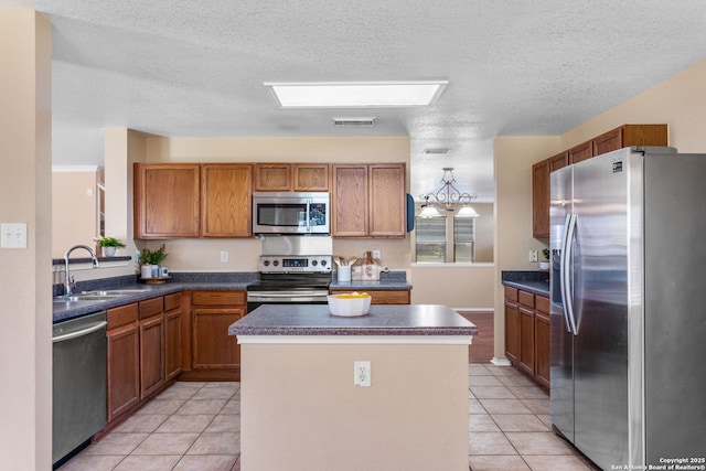 kitchen with brown cabinetry, dark countertops, appliances with stainless steel finishes, a center island, and a sink