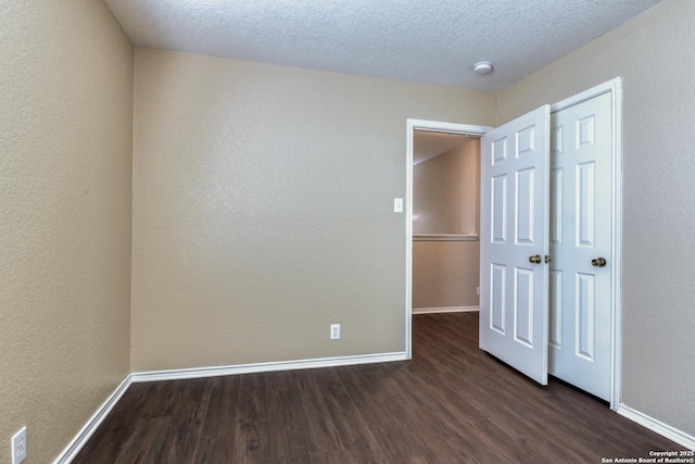 unfurnished bedroom featuring dark wood finished floors, a textured ceiling, and baseboards