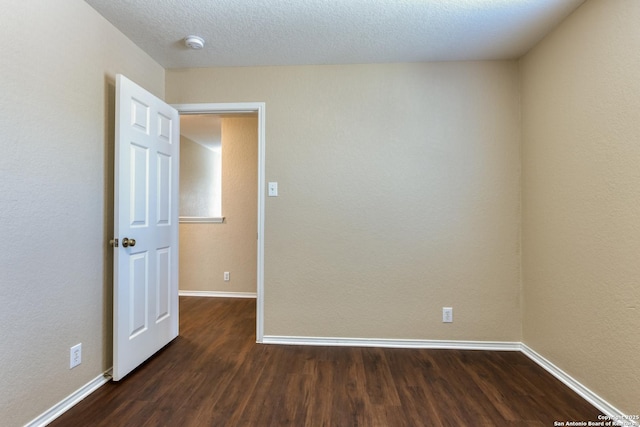 unfurnished room featuring baseboards, dark wood finished floors, and a textured ceiling