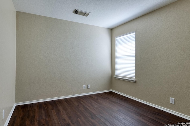 empty room featuring baseboards, visible vents, dark wood finished floors, and a textured wall