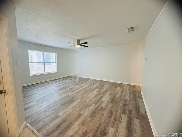 empty room with a textured ceiling, light wood-style flooring, visible vents, baseboards, and crown molding