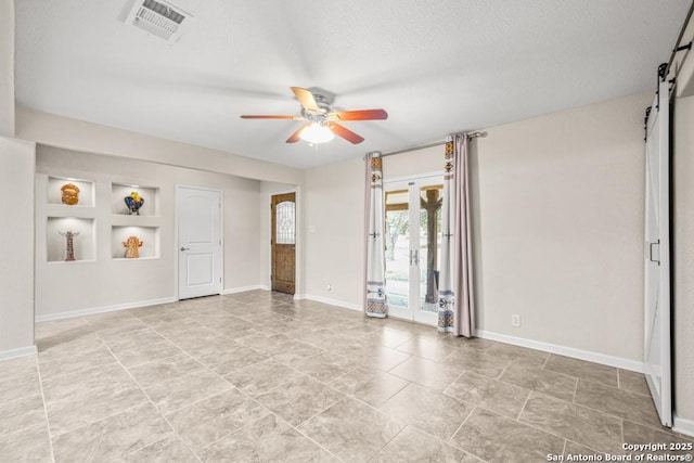 spare room featuring a barn door, visible vents, baseboards, ceiling fan, and built in shelves