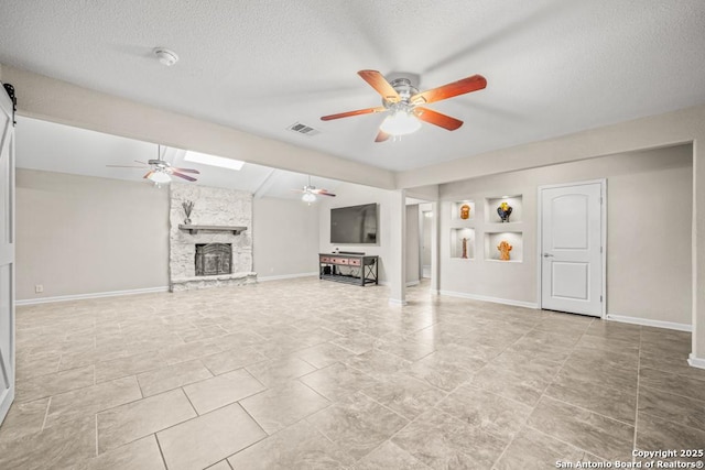 unfurnished living room featuring visible vents, a ceiling fan, a stone fireplace, a textured ceiling, and baseboards