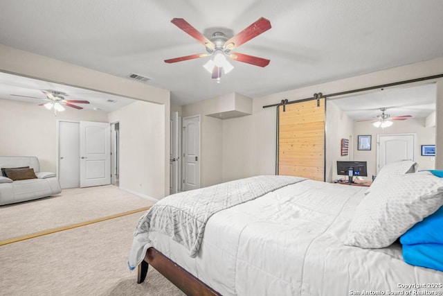 carpeted bedroom with a ceiling fan, a barn door, visible vents, and baseboards