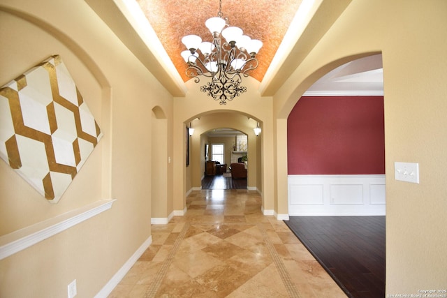 hallway with baseboards, arched walkways, lofted ceiling, a decorative wall, and a notable chandelier