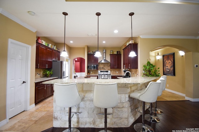 kitchen with arched walkways, a breakfast bar, appliances with stainless steel finishes, a peninsula, and wall chimney exhaust hood