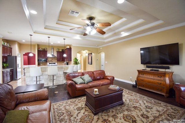 living area with dark wood-style floors, a tray ceiling, arched walkways, visible vents, and ceiling fan