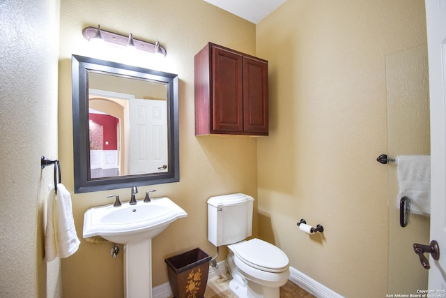 half bath with toilet, baseboards, and a sink