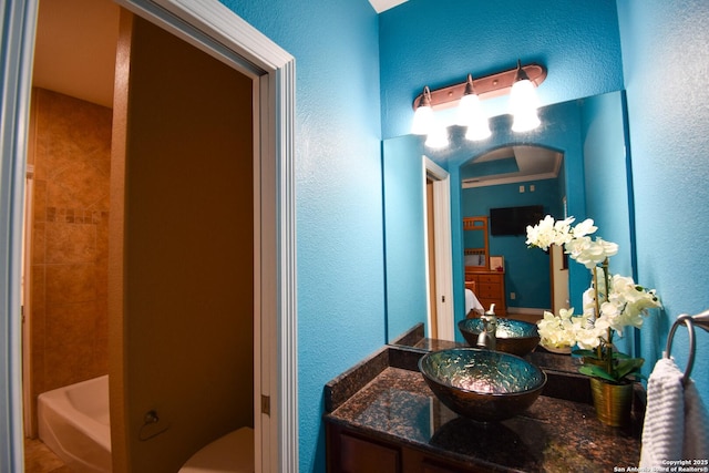 full bathroom featuring a textured wall, vanity, toilet, and a bathing tub