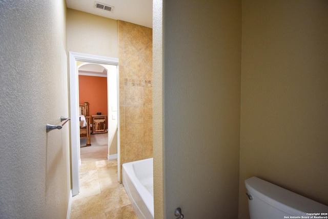 bathroom with toilet, a textured wall, a bathtub, and visible vents