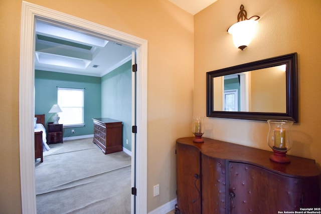 hall featuring ornamental molding, a tray ceiling, light colored carpet, and baseboards