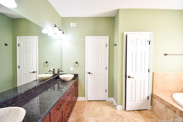 bathroom featuring double vanity, tiled bath, baseboards, and a sink