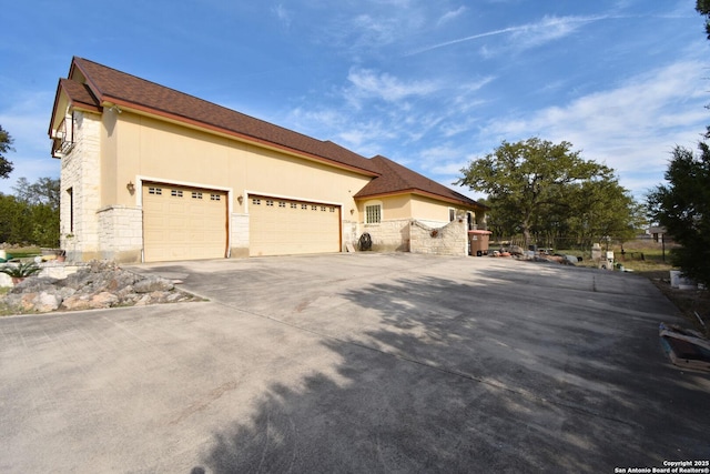 view of home's exterior with an attached garage, fence, concrete driveway, stone siding, and stucco siding