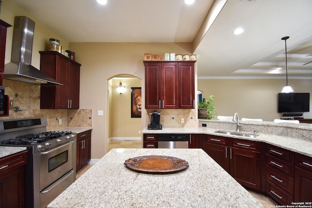 kitchen with arched walkways, wall chimney exhaust hood, light stone counters, appliances with stainless steel finishes, and a sink